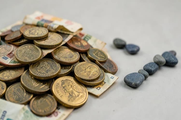 Moedas e notas de dinheiro empilhadas em frente a um gráfico de linha ascendente.