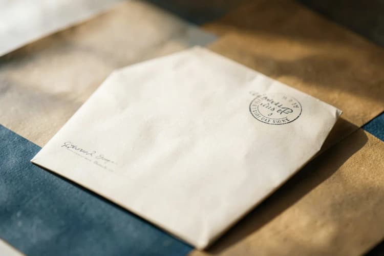 Uma mão segurando uma carta com um selo, pronta para ser enviada.