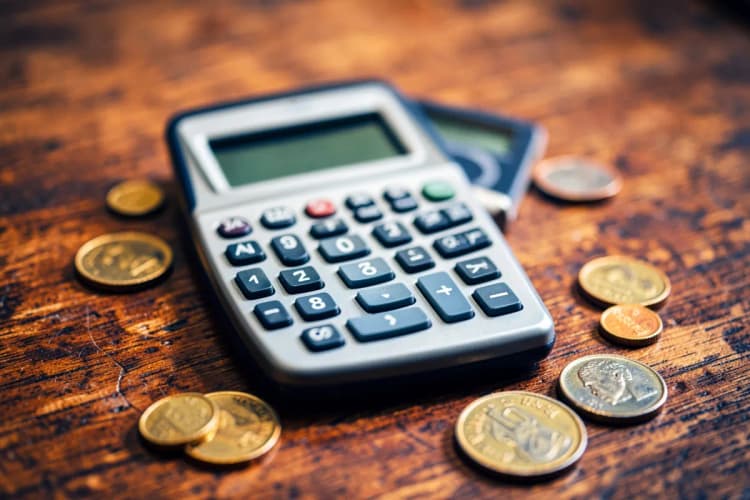 Uma calculadora e algumas moedas em uma superfície de madeira.