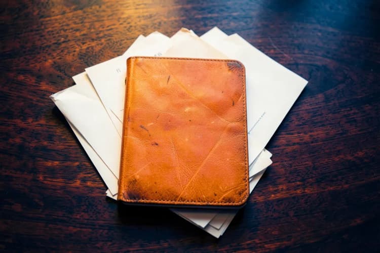 Um bloco de notas fechado com alguns papéis ao lado em uma mesa de madeira escura, plano detalhe, luz de escritório vinda de cima, sem pessoas.