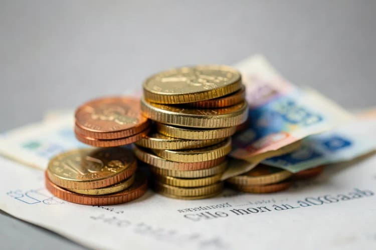 Uma pilha de moedas de ouro e notas de dinheiro em cima de um documento oficial.