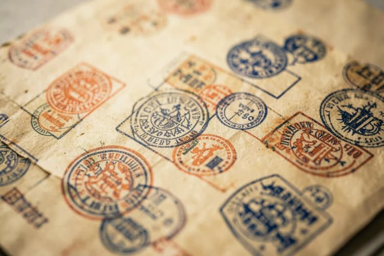 Uma mão segurando uma lupa sobre um documento com selos e carimbos, simbolizando a consulta e verificação de direitos a benefícios.